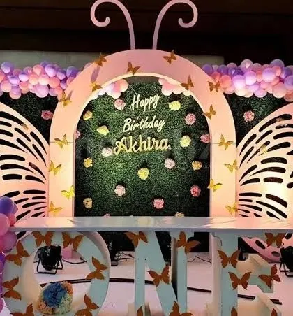 A stunning butterfly themed birthday setup with large, elegant butterfly wings framing a green hedge backdrop, perfect for a first birthday.