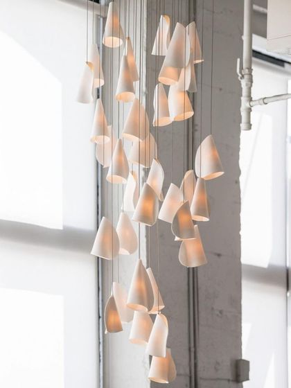 A tall, cascading installation of Bocci 21 pendants in a double-height space with large windows, accentuating the room's verticality.