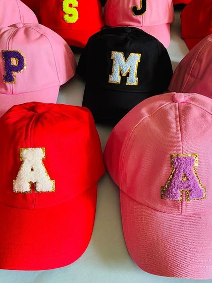 An array of custom initial caps in multiple colors, showcasing the different letter patches available. These are a popular choice for bulk orders for party return favors.