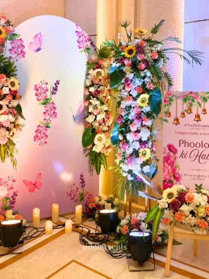 The welcome area for the 'Phoolon ki Haldi', with a custom sign, colorful floral arrangements, and arched panels creating a festive and inviting atmosphere.