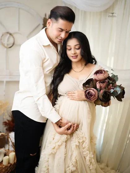 The mother-to-be holds a bouquet of flowers while her partner embraces her from behind. This pose adds a touch of romance to the earthy, natural setting.