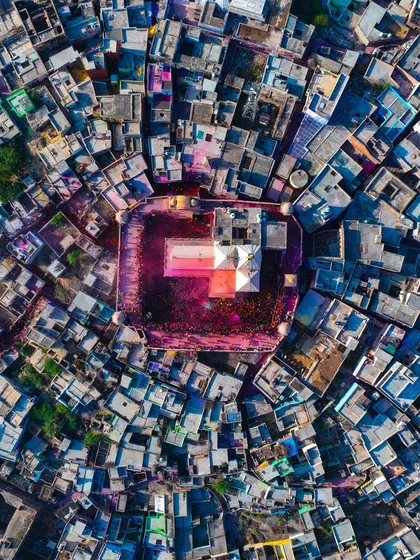 A closer top-down shot of the temple courtyard during Holi. You can see the ground is completely covered in a carpet of pink and red colors.