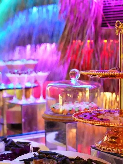 A vibrant dessert station with a tiered stand of sweets, set against a backdrop of colourful party lights.