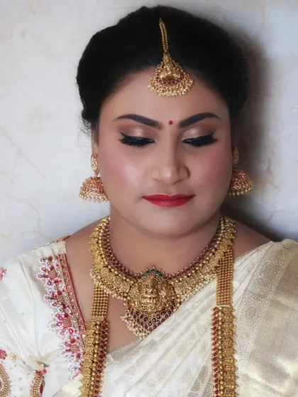 A close-up of a flawless muhurtham makeover. The bride's skin is radiant, and her makeup features classic winged eyeliner and a red lip, perfectly complementing her white silk saree and traditional temple jewellery.