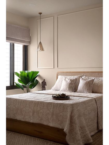 Another view of the minimalist guest bedroom. The clean lines of the wall moulding, the natural texture of the cane headboard, and the soft lighting create a warm and welcoming ambiance for visitors.