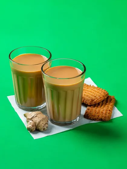 Two glasses of Indian masala chai with ginger and biscuits. This shot for Bistro by Blinkit evokes a sense of comfort and tradition.