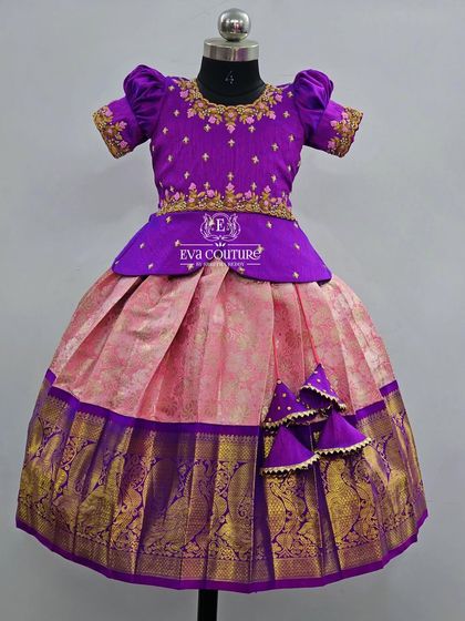 A beautiful Kanchi Pattu lehenga in purple and pink. The blouse has a simple peplum design, and the skirt has a traditional gold zari border with peacock motifs.
