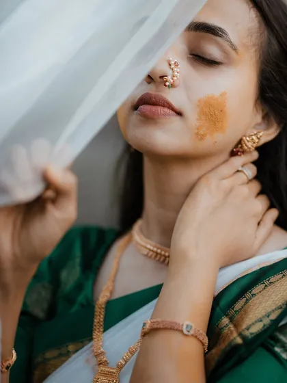An artistic and serene portrait of a bride during her Haldi, with a sheer veil partially covering her face.