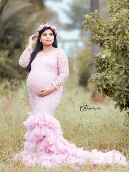 A beautiful solo portrait in a pink lace gown with a ruffled train and a floral crown, set in a lush green field.