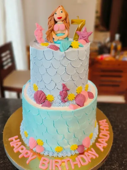 A magical two-tier mermaid themed cake with fondant scales, shells, and a handcrafted mermaid topper.