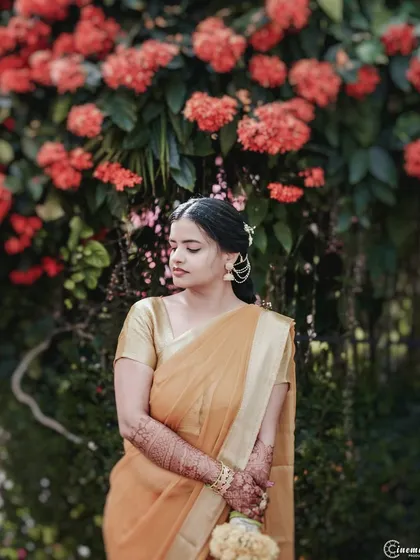 A serene portrait of the bride during her Haldi ceremony, standing before a wall of beautiful orange flowers that complement her sari.