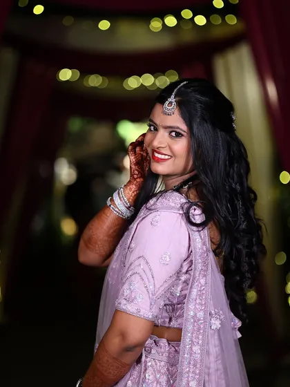 The pure joy of a reception-ready bride. For Isha's celebration, we went with a glamorous yet elegant look, featuring a bold red lip and soft, radiant makeup that complemented her lavender lehenga and let her personality shine.