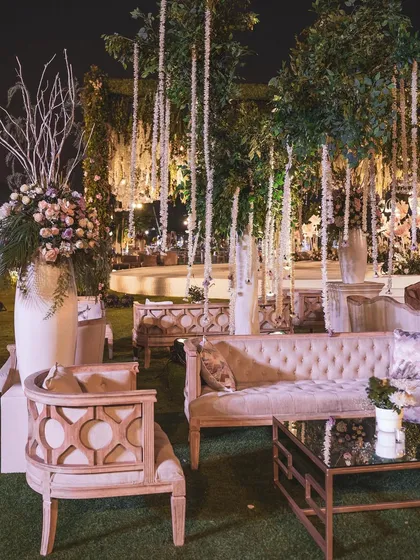 Another view of the reception lounge seating, highlighting the elegant wooden-accented chairs and plush sofas. Hanging floral strings and intricate details create a layered and luxurious feel.