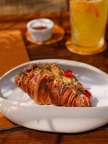 A close-up of a savory croissant, filled with cheese and topped with fresh chili, a warm and indulgent treat.