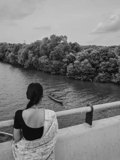 A beautiful, scenic shot of a woman in a saree looking out at the river. It evokes a sense of longing and contemplation.