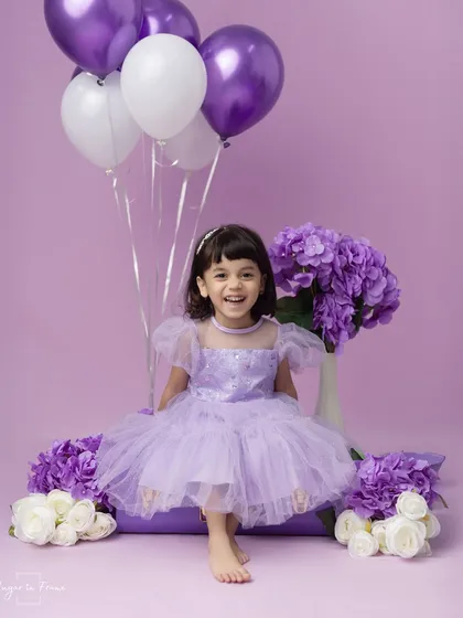 Celebrating a third birthday in style. This little girl is all smiles in her beautiful lavender dress, surrounded by matching balloons and flowers.