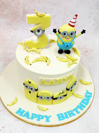 This Minions Banana Cake is full of playful energy, featuring a minion in a party hat, a minion-themed number '3', and lots of edible bananas.