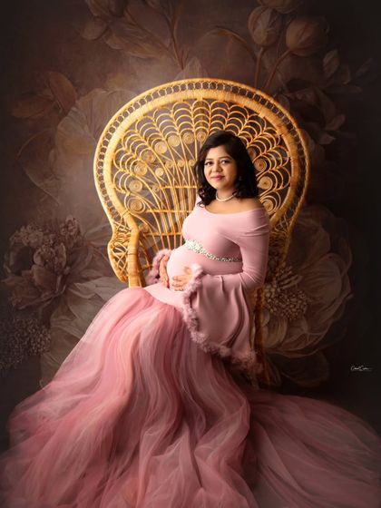 Seated gracefully on the peacock chair, this mom-to-be looks serene in a fitted pink gown with a tulle train, set against a floral backdrop.