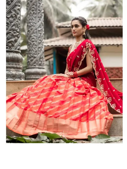 The full view of the orange-red brocade lehenga, showcasing its beautiful flare and how it drapes elegantly when seated. A timeless choice for any bride.