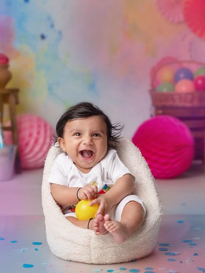 A joyful baby boy laughs heartily during his Holi-themed photoshoot, surrounded by bright colors.
