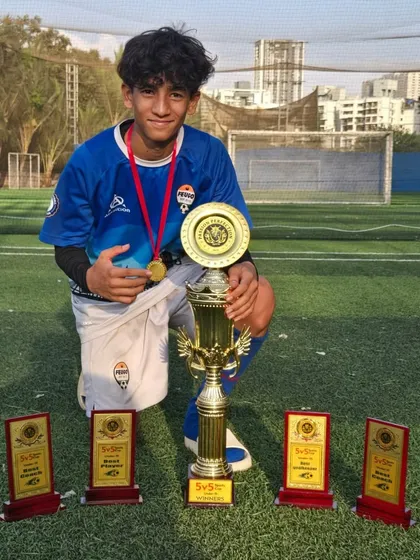 A smiling U15 player with his team's championship trophy and individual awards.