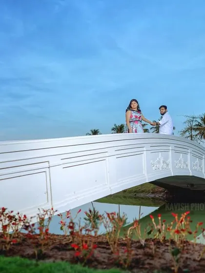 A grand, scenic pre-wedding photo of a couple on a white bridge, with palm trees and a clear blue sky creating a picturesque setting.