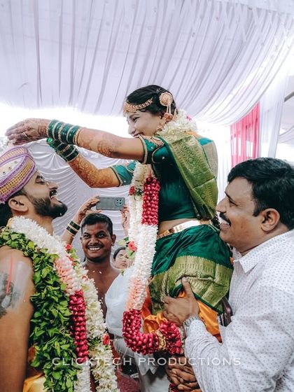 A joyful and significant ritual during a South Indian wedding, where the bride is lifted high to place the garland on the groom, surrounded by supportive family.