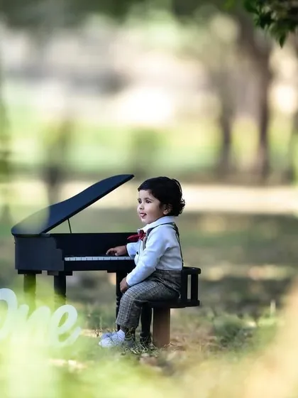 A side profile of the birthday boy sitting at the mini piano, framed by trees in the background. This composition creates a lovely, scenic portrait.