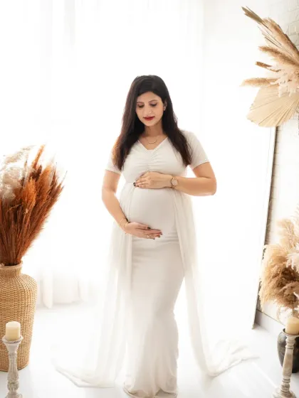 A classic three-quarter portrait of an expecting mother in a white gown. Her gentle smile and hand on her bump convey a sense of calm and happiness.