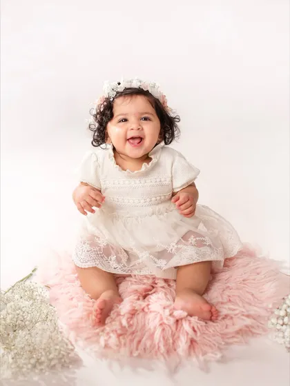 A joyful, open-mouthed smile from an eleven-month-old sitting on a pink rug. Her personality is really starting to shine as she approaches her first birthday.
