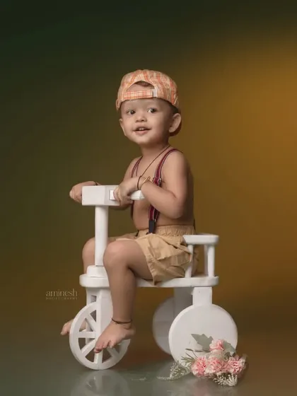 A playful shot of a little boy on a white tricycle against a moody, gradient background. The simple props allow his personality to shine through.