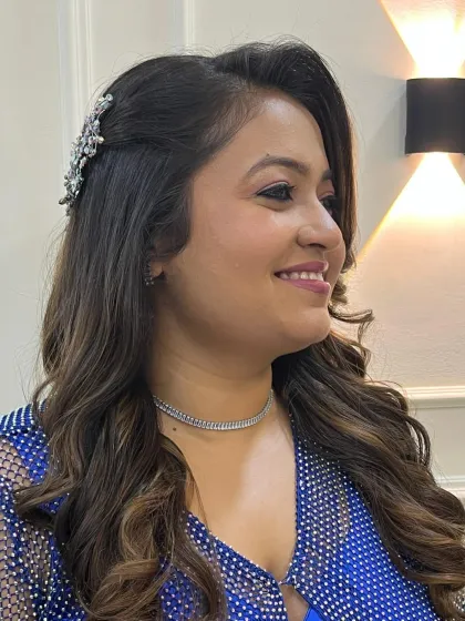 A soft and radiant party look. The client is glowing in a royal blue outfit, with her hair in soft waves and a beautiful hair accessory.