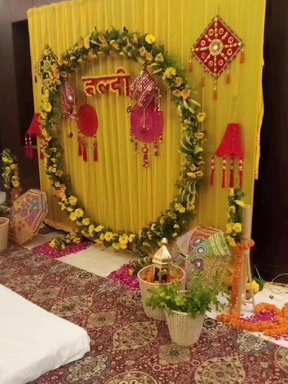 An indoor Haldi setup with a circular marigold backdrop and traditional Rajasthani hangings. The yellow fabric draping and patterned carpet complete the festive look.