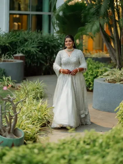 An outdoor shot of the bride in her Sangeet outfit. The natural light highlights the delicate texture of the organza skirt and the sparkle of the zardozi embroidery.