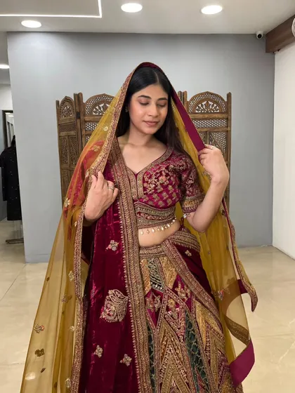 This unique multi-panelled velvet lehenga combines shades of maroon and green with heavy traditional embroidery.