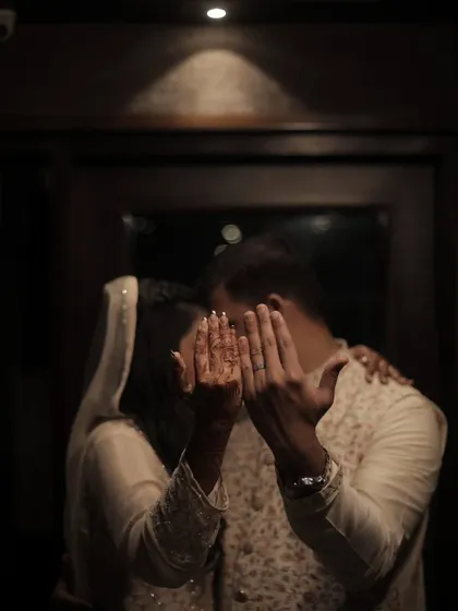 A creative and intimate shot of an engaged couple, their faces hidden by their hands, drawing focus to the henna and the commitment they've made.