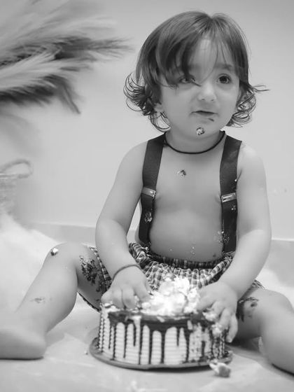 A cake smash scene in black and white, focusing on the textures of the cake and the child's messy, happy expression.
