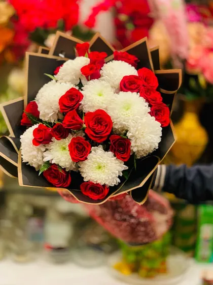 A beautiful bouquet combining classic red roses with fluffy white chrysanthemums. The contrast in color and texture makes this a visually striking arrangement, presented in a modern black wrap.
