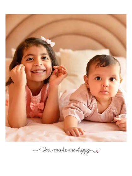 Two sisters, one big and one small, lying on a bed in coordinating pink outfits. A simple, sweet portrait that captures their budding friendship.