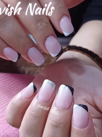 A chic, angular French manicure on short, square nails, using both black and silver glitter for a modern, color-blocked look.