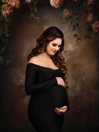 A classic and moody portrait against a painterly backdrop with floral elements. The client's simple black off-shoulder gown and serene expression create a timeless and artistic image.