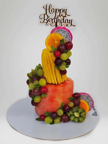 A healthy and refreshing two-tier cake made entirely from fresh watermelon. It's decorated with a cascade of grapes, kiwi, and dragon fruit, perfect for a diet-conscious celebration.