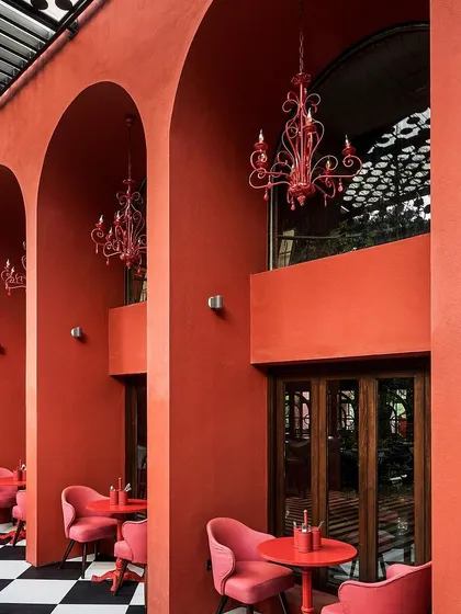 The outdoor seating area at Suzy Q features a striking monochrome design. The bold red walls with repeating arches, checkerboard flooring, and custom red chandeliers create a vibrant, high-contrast space that is both playful and sophisticated.