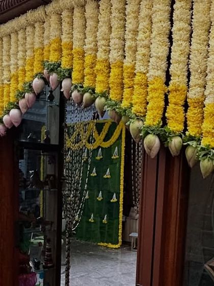 A close-up of a traditional door decoration, or 'thoranam', made with yellow and white flowers and mango leaves for an auspicious event.