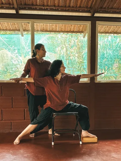 In our 300-hour course, you'll master prop usage for therapeutic benefit. Here, a student practices a modified Warrior II pose using a chair for support, learning how to build strength and alignment safely.