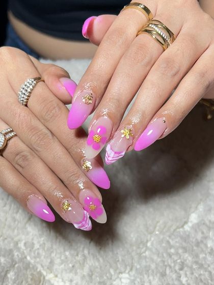 A close-up of the detailed 3D flower and gold charm on these stunning pink ombre nail extensions.