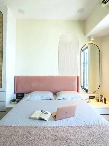 A personalized and comfortable space featuring a soft pink headboard, an arched wall detail, and a sleek bedside table.