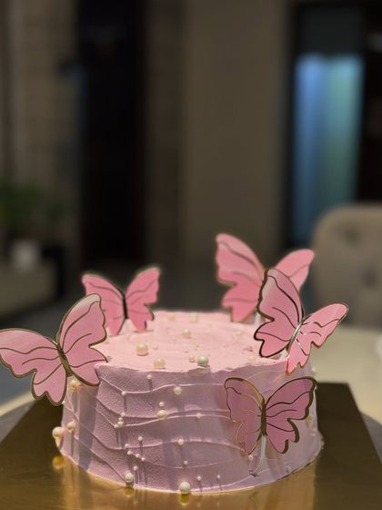 A whimsical butterfly-themed cake. The light pink frosting is adorned with delicate pearl details and beautiful pink butterfly toppers, creating a dreamy and magical look.