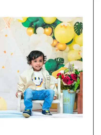 This little boy, dressed in a cool jacket and jeans, gives a sweet smile during his second birthday session. The setup with balloons and flowers creates a perfect celebratory atmosphere.
