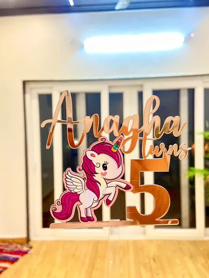 The unicorn topper for Anagha, seen from a different angle, highlighting its 3D effect against an indoor background.